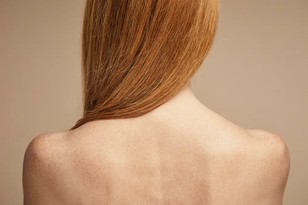 Espalda descubierta de mujer con cabello pelirrojo sobre fondo beige